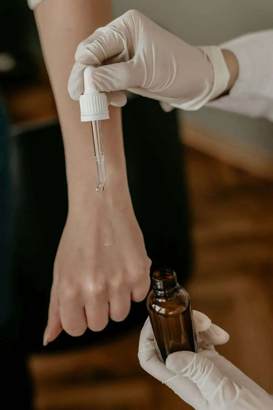 Dłonie w rękawiczkach nakładają serum z pipety